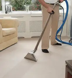 Professional carpet cleaner using a hot-water extraction wand and hose machine in a living room in Fort Wayne, IN.