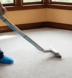 Steam carpet cleaning technician using a hot-water extraction wand on a residential carpet, wearing blue protective shoe covers Fort Wayne, IN.