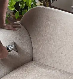Professional upholstery cleaner deep-cleaning a fabric sofa with a handheld extraction tool and hose Fort Wayne, IN.
